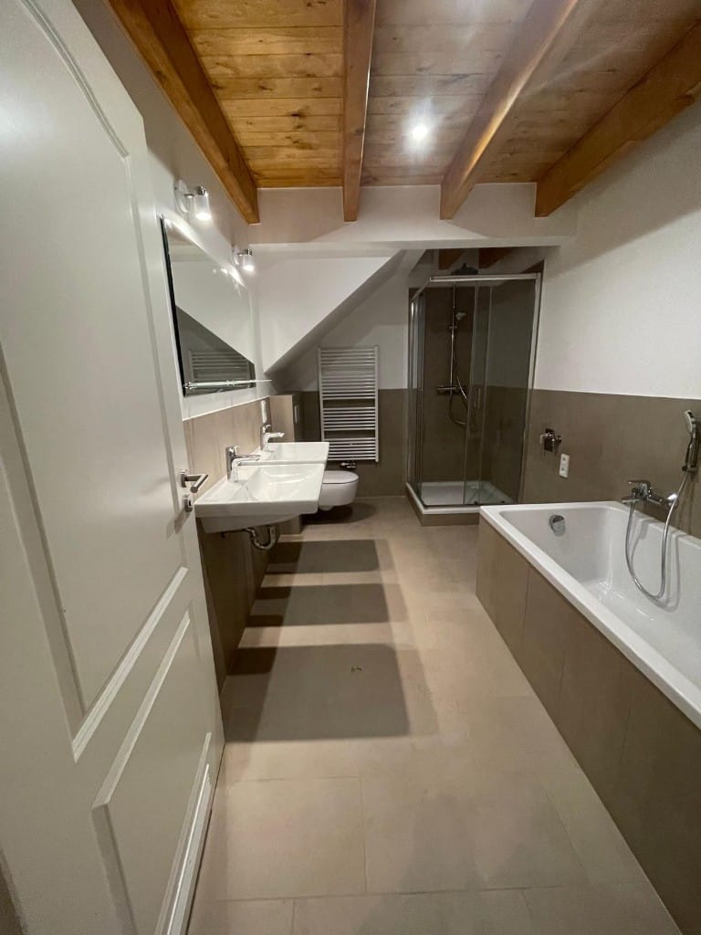 Komplett saniertes Badezimmer in Hamburg mit Holzbalkendecke, Doppelwaschtisch, Badewanne und Glasdusche.